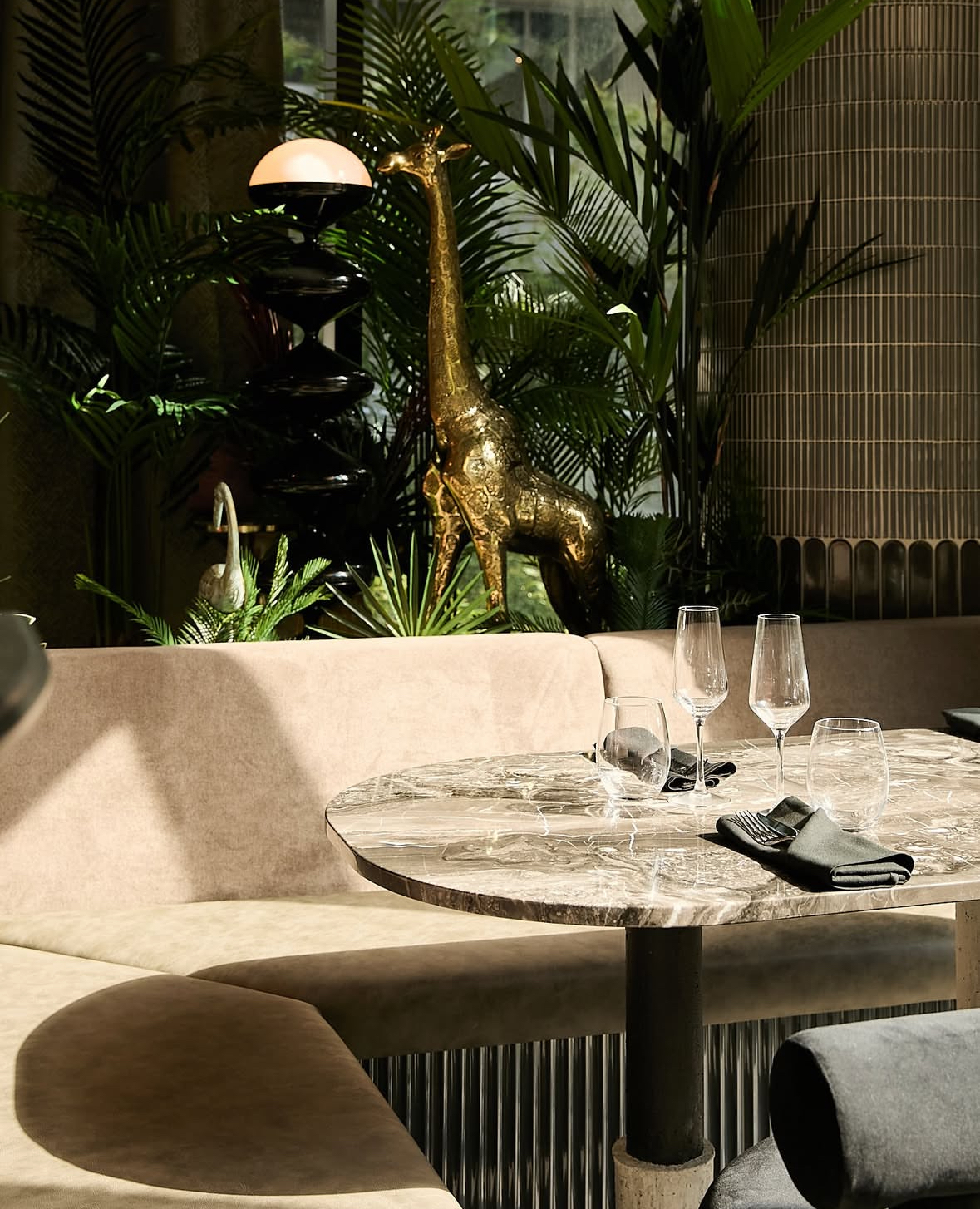 Banquette dining nook en velours taupe avec table ronde en marbre et décor tropical, projet commercial
